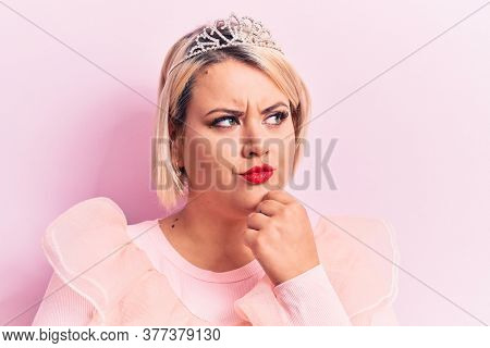 Beautiful blonde plus size woman wearing pincess tiara with diamonds over pink background thinking concentrated about doubt with finger on chin and looking up wondering