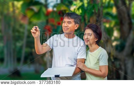 Asian Middle-aged Couple Talking And Designing Garden Plan Together In Backyard.