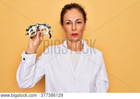 Middle age senior oculist woman holding optometrical glasses for vision correction with a confident expression on smart face thinking serious