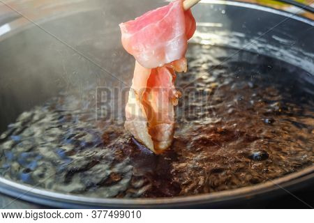 Hand Using Chopsticks Pick Raw Sliced Pork Over The Hot Pot Soup With Smoke For Shabu Shabu Or Sukiy