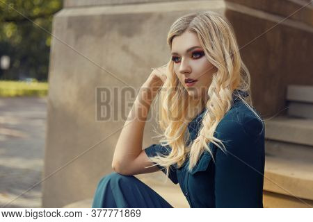 The Girl Sits Alone Near The Campus On The Stairs And Looks Into The Distance. Gorgeous Blonde With