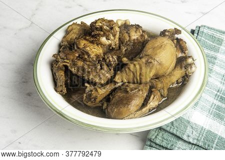 A Serving Of Filipino-style Chicken Adobo Dish In A Bowl With Green Napkin Set On A Marble Tabletop.