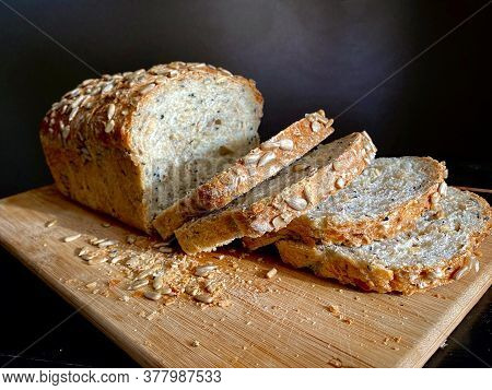 Loaf Of German Traditional Multi-cereal Bread Vollkornbrot, Partially Cut Into Slices On A Wooden Cu