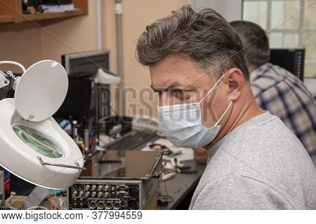 Portrait Of A Man 40-45 Years Old In A Medical Mask At Work In A Computer Repair Shop.