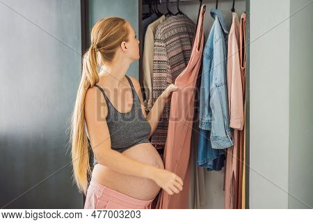 A Pregnant Woman Has Nothing To Wear. A Pregnant Woman Stands In Front Of A Closet With Clothes And 