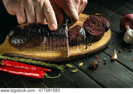 The Chef Cuts Blood Sausage On A Cutting Board For Dinner With A Knife. Cooking A National Dish On T