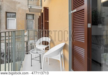 Table And Chairs Stand On An Unglazed Balcony Overlooking The Courtyard And Other Balconies And Fire