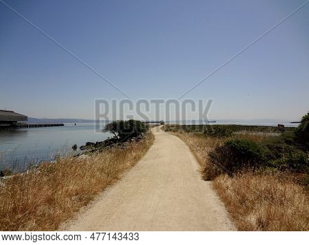 A Path Leads Out To Rocky Point At Heron's Head Park In San Francisco, California. In The Distance, 