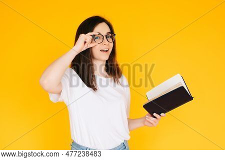 Portrait Of A Happy Young Woman Wearing Glasses And White T-shirt, Immersed In Reading A Book With A