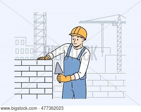 Positive Male Worker In Uniform And Helmet Building House With Bricks. Smiling Man Engineer Busy Lay