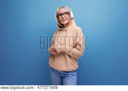 Stylish 60s Granny With Gray Hair Learns Again And Listens To Music With Headphones On Studio Backgr