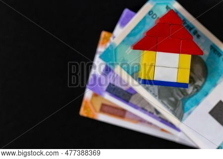 Top Close Up Shot Of A Toy House On Money Notes Placed Over Black Background.