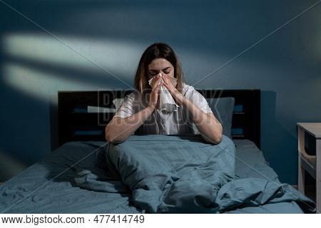 Sick Young Woman In Bed Blowing Nose In Napkin At Night. Lady Suffering Cold And Flu Having Temperat