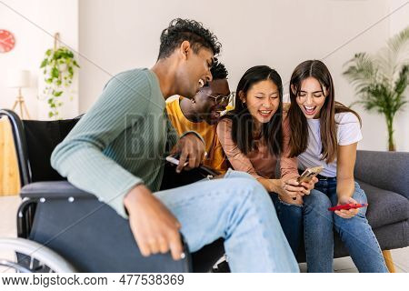 Young Group Of People Using Mobile Phone Device Sitting Together On Sofa At Home. Inclusion And Dive