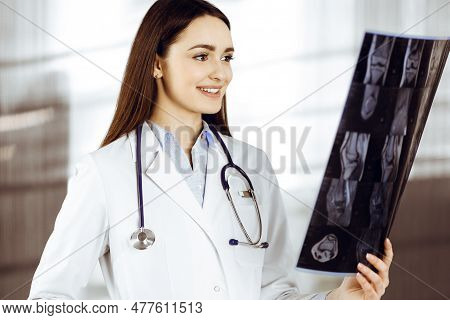 Professional Young Woman-doctor Is Looking At Her Patients Roentgenogram. Physician At Work In A Cli