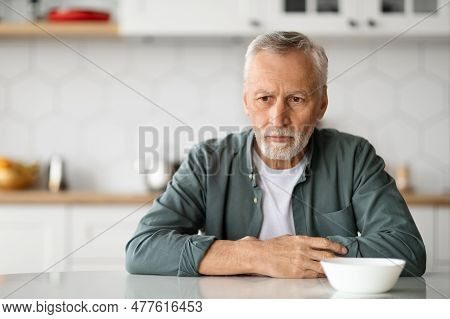 Depression In Seniors. Upset Elderly Man Sitting At Table In Kitchen