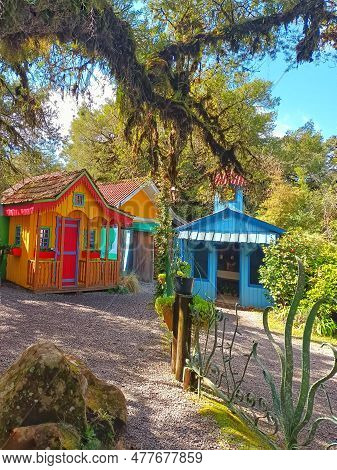 Two Colorful Rustic Houses In The Middle Of Green Trees On A Sunny Day And Blue Sky