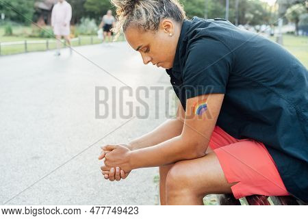 Sad Frustrated Lesbian Woman With Lgbtq Rainbow Tattoo On Her Hand Sitting On The Park Bench Alone. 