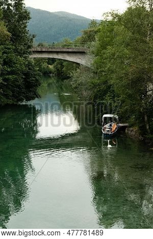 Small Boat Surrounded By Lovely Green Trees At The Mangfall River With A Bridge Over It In Bavaria, 