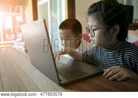 Two Asian Children Learning To Use Computer Laptop At Home Living Room