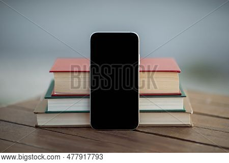 Smartphone With Empty Screen Standing Near Books On Table Outdoors
