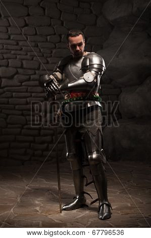 Medieval Knight posing with sword in a dark stone background