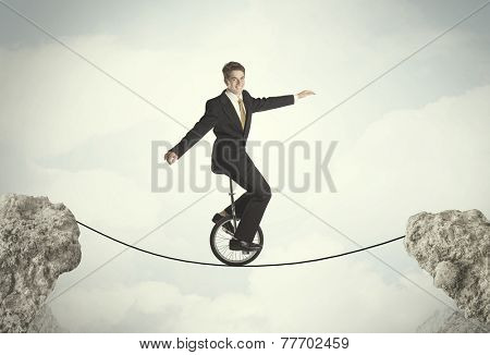 Brave business man riding an mono cycle between cliffs concept