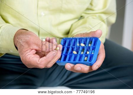 Senior man uses a pill organizer to prepare his medication for the week.