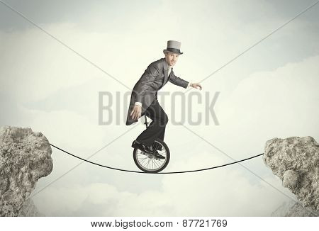 Brave business man riding an mono cycle between cliffs concept