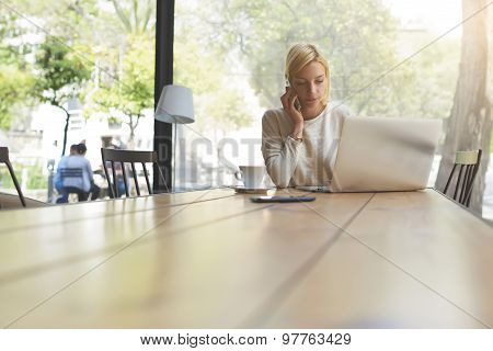 Attractive young female having smartphone conversation in modern loft interior with big windows