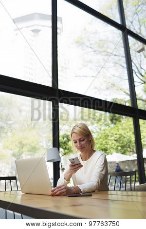 Businesswoman or young freelancer reading text message on smartphone sitting front open computer