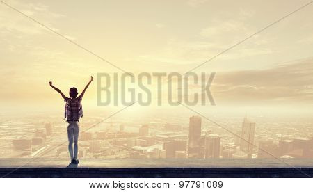 Rear view of girl with hands up facing sunrise abone city