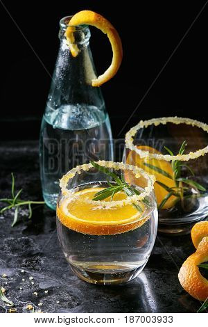 Tonic water cocktail with rosemary and orange. Two glasses and bottle with zest sugar and bubbles over black texture background. Refreshing beverage alco non alcohol