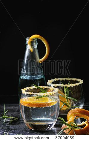 Tonic water cocktail with rosemary and orange. Two glasses and bottle with zest sugar and bubbles over black texture background. Refreshing beverage alco non alcohol