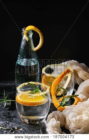 Tonic water cocktail with rosemary and orange. Two glasses and bottle with zest sugar and bubbles with textile gauze over black texture background. Refreshing beverage alco non alcohol