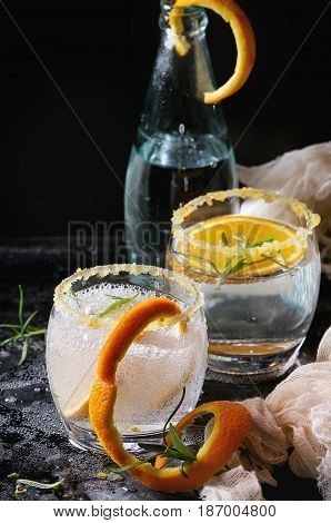 Tonic water cocktail with rosemary and orange. Two glasses and bottle with zest sugar and bubbles with textile gauze over black texture background. Refreshing beverage alco non alcohol
