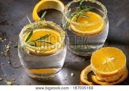 Tonic water cocktail with rosemary and orange. Two glasses with zest sugar and bubbles with textile over dark texture metal background. Refreshing beverage alco non alcohol