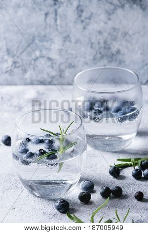Tonic water cocktail with rosemary and blueberries. Two cold glasses over gray blue texture background. Refreshing beverage alco non alcohol