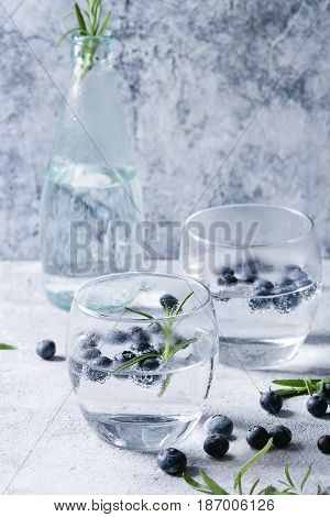 Tonic water cocktail with rosemary and blueberries. Two cold glasses and bottle with bubbles over gray blue texture background. Refreshing beverage alco non alcohol