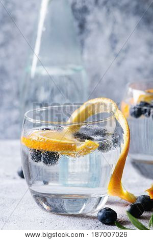 Tonic water cocktail with rosemary, blueberries and orange. Two cold glasses and bottle with zest and bubbles over gray blue texture background. Refreshing beverage alco non alcohol. Close up