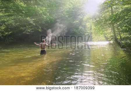Man having a bath in Cerna river with open arms, in front of the sun, in Herculane resort, Romania