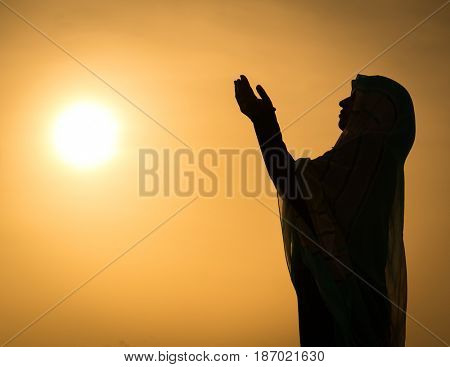 Silhouette Muslim Arabic woman praying with her hands up