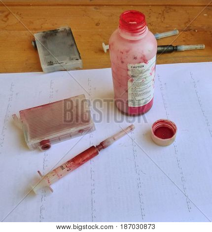 Process of ink cartridge refill - toner in open bottle and syringe. On dirty paper. Jet printer maintenance.