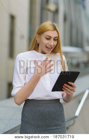 Happy business woman using tablet pc in front of office building.
