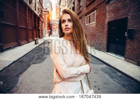 Beautiful lonely girl walking on epmty city strret looking up to the side. City urban people lifestyle concept.