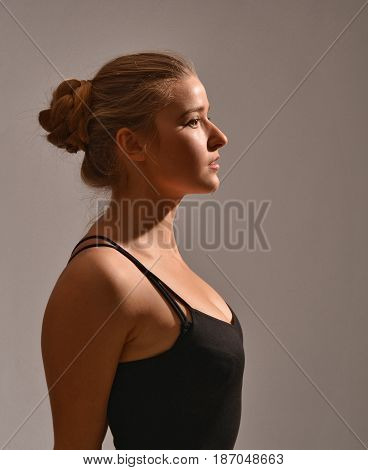 Half-length profile of young girl in black T-shirt with open shoulders posing in studio on grey. Her sight is directed forvard. Her armsbehind back, hair pulled. Dance, ballet, fashion.