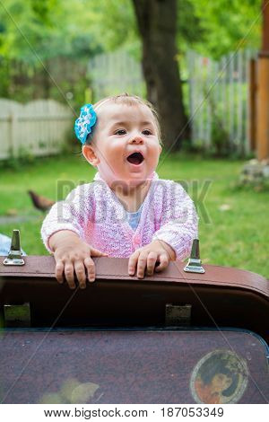 Baby sitting near suitcase in the summer garden