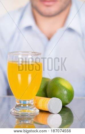 Handsome guy behind of Lemon, pills of vitamin C and a glass of vitamin C dissolved over the table.