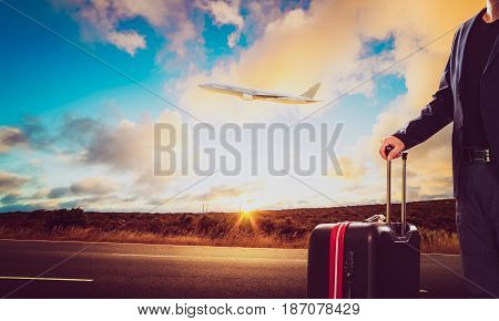 Business man with traveling luggage standing against landscape scene and passenger jet plane flying over sky .