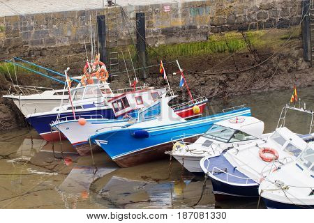 Motor boats of the boat in a marine during an outflow. Low water level has bared seaweed on a stone wall. Boats lie on one side